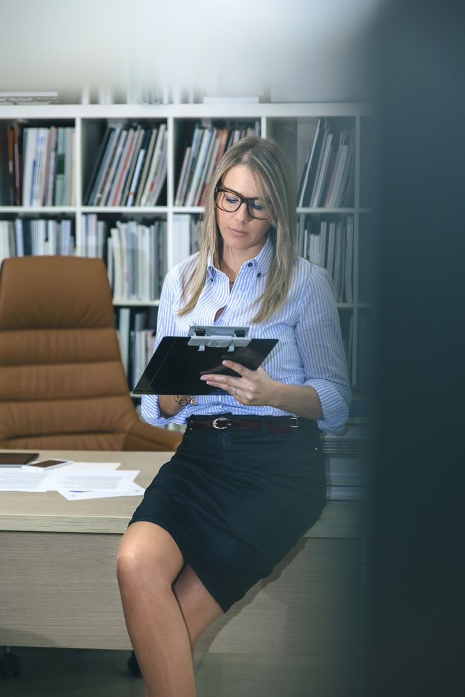 Woman taking notes with clipboard in office seen behind door