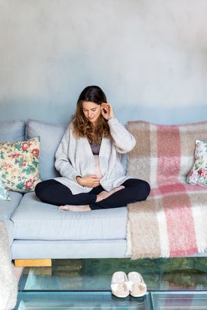 Pregnant woman relaxing at home sitting cross legged on sofa