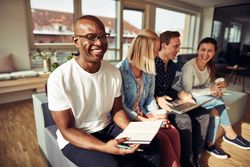 Portrait of happy Black man on couch with his notebook and work colleagues