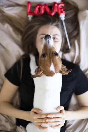 Woman lying on her back on a bed with her dog on her chest and a love balloon near her head