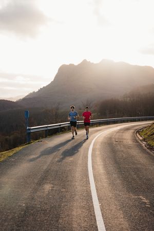 Sportsmen running on asphalt road in mountains