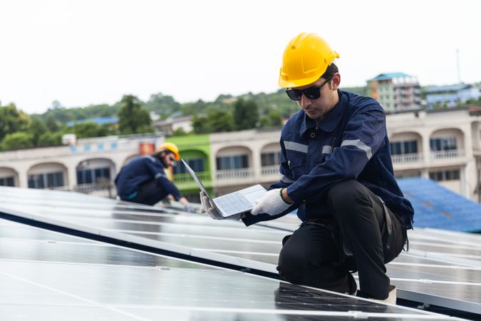 Engineer checking solar cell  or photovoltaic cell by computer laptop installed on the roof of the factory. Technician worker repair or inspect the system. Industrial renewable energy concept