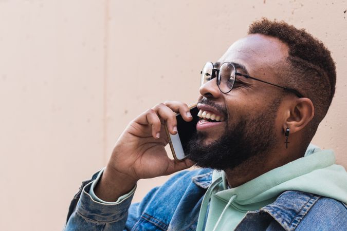 Cheerful Black man talking on phone near wall