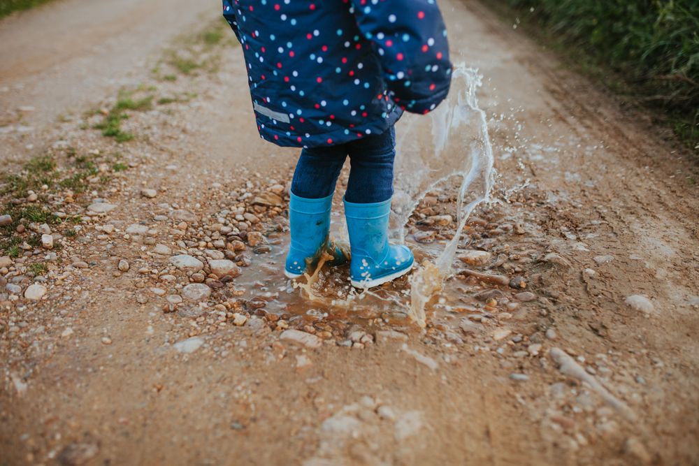 Child in rainboots splashing in puddle