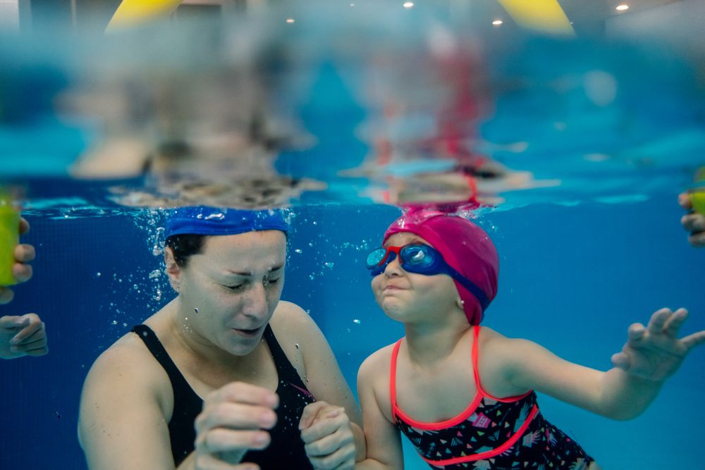 Cheerful girl underwater swimming in pool with mother