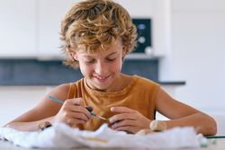 Smiling boy painting pebble with gouache