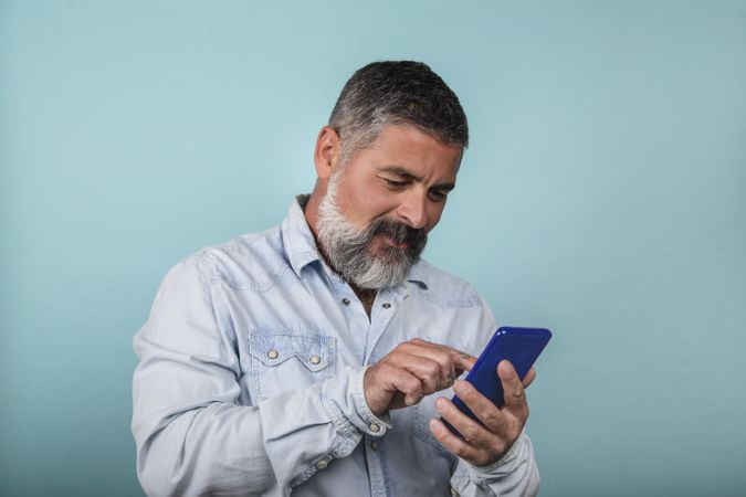 Middle aged man using smartphone standing against blue background
