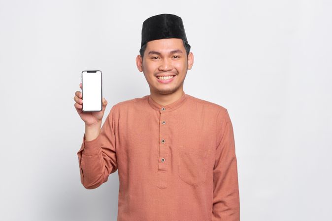 Muslim man in kufi hat smiling with mobile phone