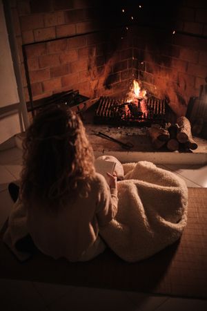 Unrecognizable woman covered with blanket sitting near fireplace