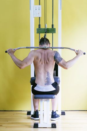Back of tattooed male using weight machine