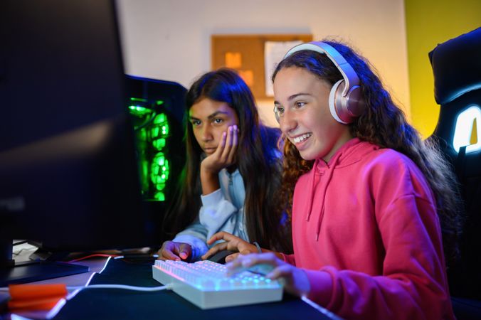 Teenage diverse sitting at table with gaming PC and playing game