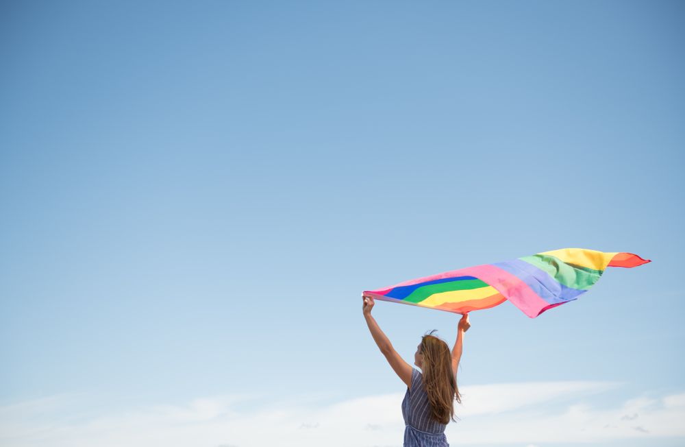 Young woman with rainbow banner against sky