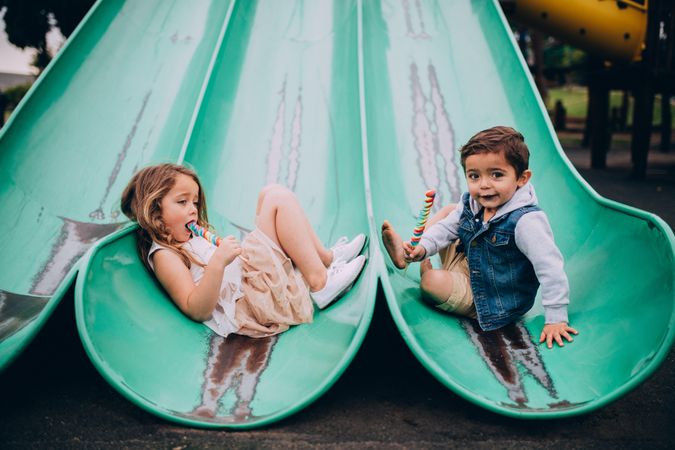 Two kids playing on a slide at a playground