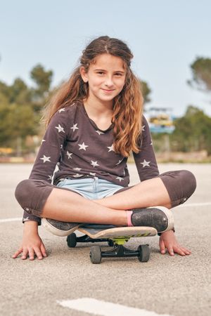 Content girl sitting on skateboard in city