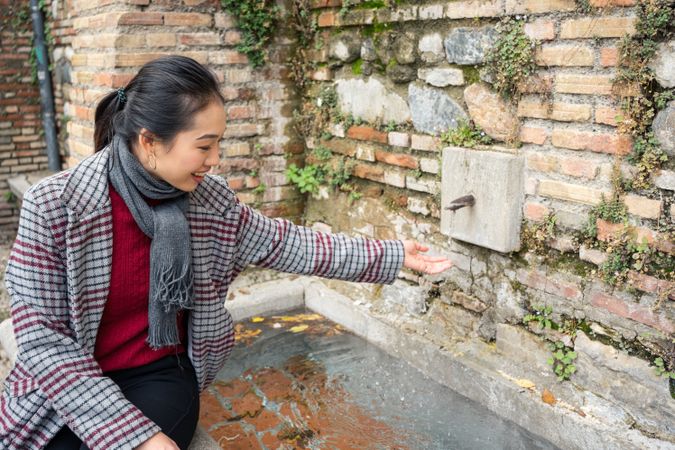 Young woman in casual clothing washing hands in street fountain