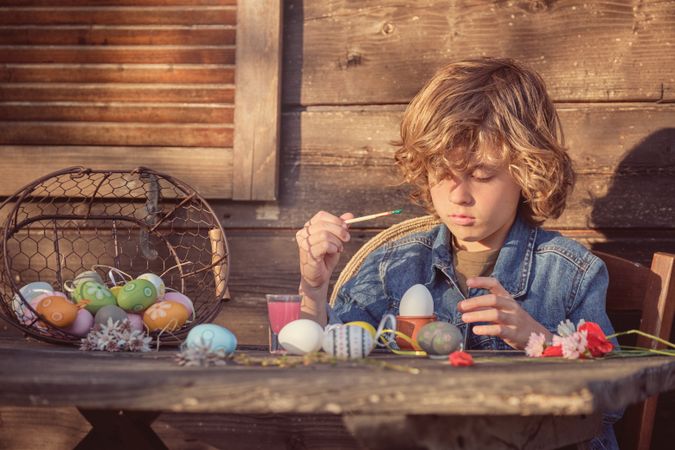 Little boy painting Easter eggs with brush