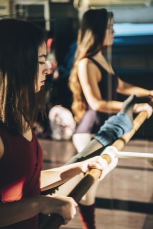 Young ballerinas training in sunny studio standing near mirror with barre.