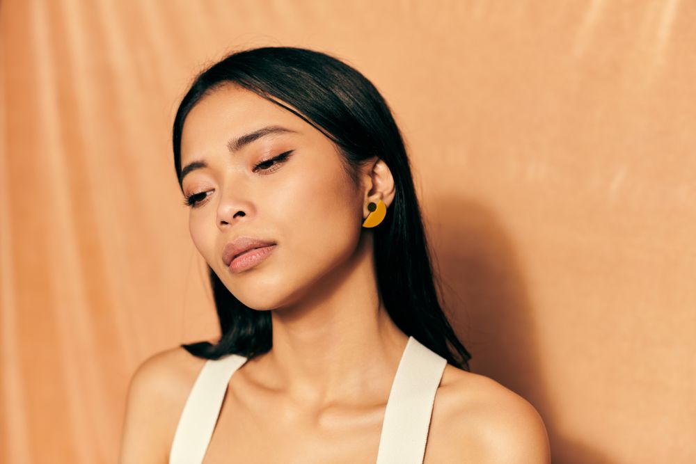 Woman with dark hair standing against peach colored backdrop looking away