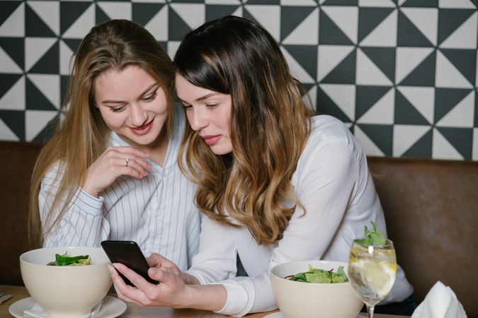 Women friends using smartphone at restaurant table