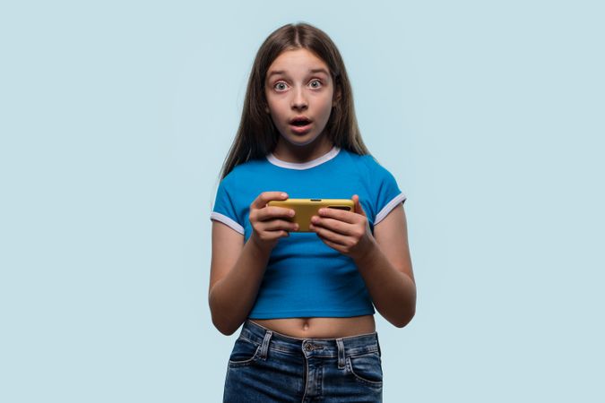 Girl looking surprised while holding smartphone, expressing shock