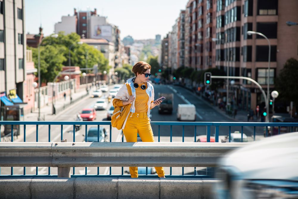 Woman with smartphone standing on road bridge