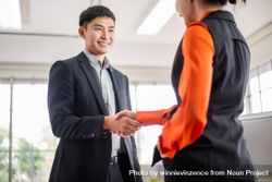Smiling Asian male in suit shaking woman’s hand 4NeX95