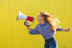 Side view of woman yelling into megaphone in checkered shirt against a yellow wall