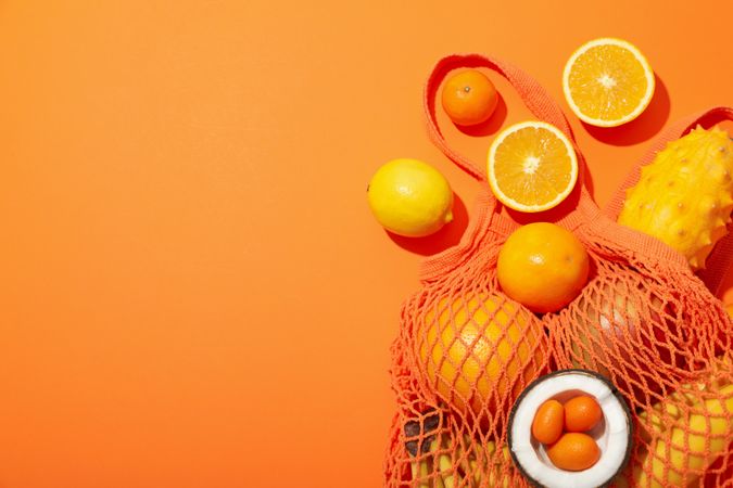 Set of tropical fruit in bag on orange background, space for text