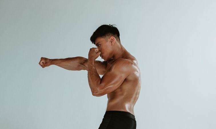 Side view of a muscular sports man training boxing moves in studio