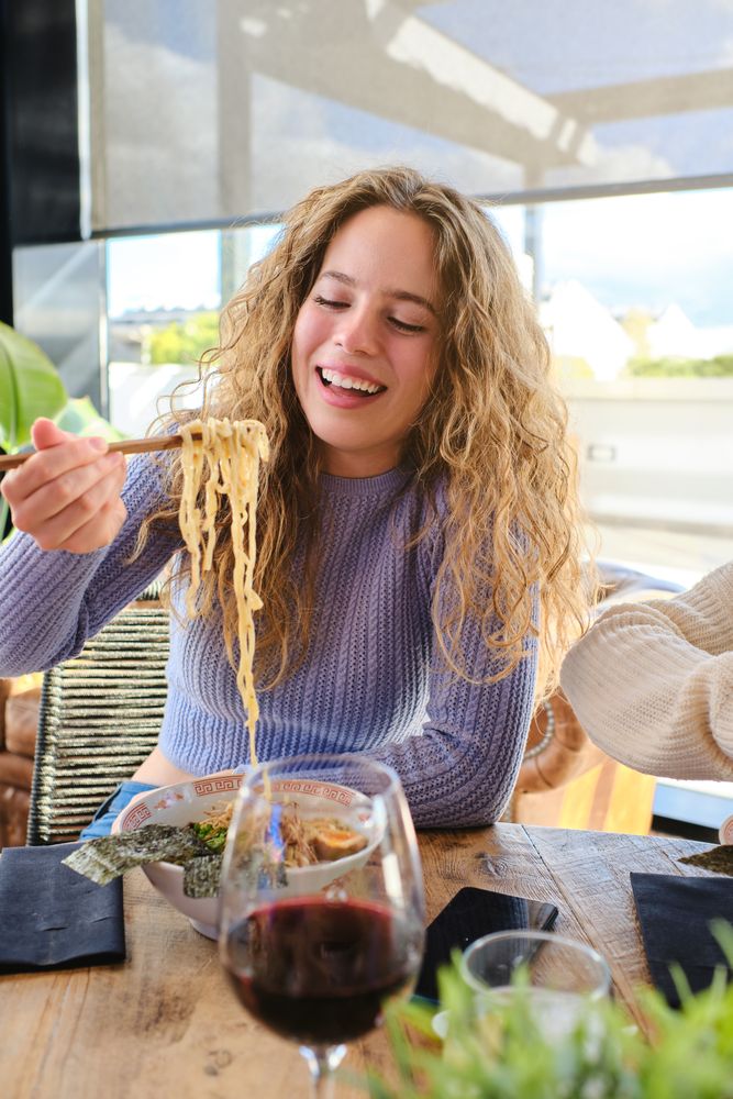 Satisfied fair haired woman eating ramen in restaurant