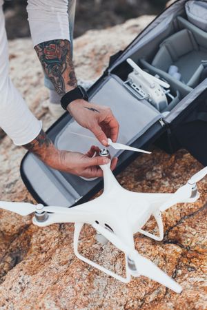 Close up of man with tattooed arms opening bag with drone equipment on a seaside cliff