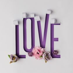 Word LOVE made of torn paper on violet background with flowers