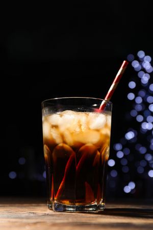 Glass with cola, lime slice and tubule against blurred lights background