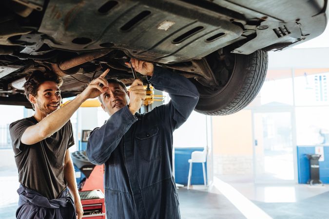 Mechanic fixing the car with coworker pointing and smiling