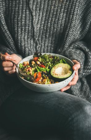 Woman in jeans and sweater eating fresh salad, vertical composition