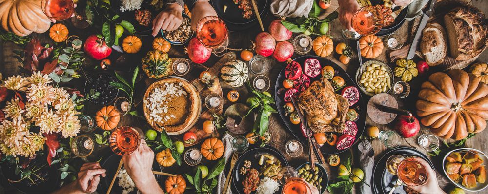 Group of people at festive table setting with roast chicken, squash, and pie, wide composition