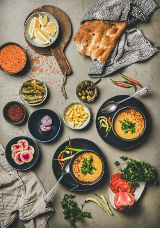 Spread of yellow lentil soup bowls, with bread, and vegetable garnishes, vertical composition