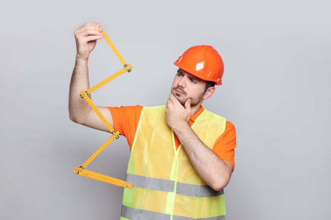 Engineer in helmet with ruler on gray background