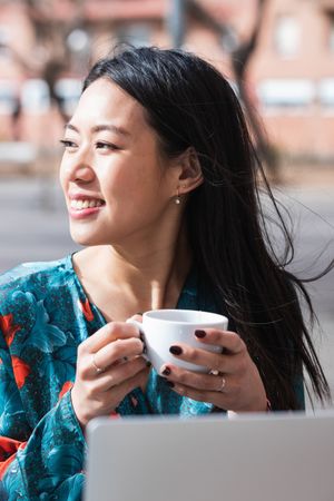 Long-haired brunette Asian woman having a coffee on a terrace of a cafe