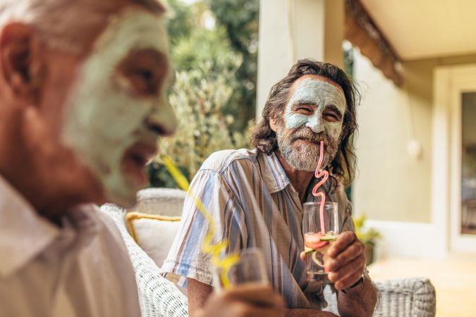 Two male friends with facial clay mask on drinking juice