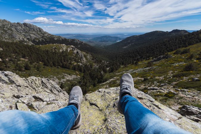 Person sitting dangling legs on stone above mountain valley