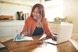 Businesswoman smiling while taking notes from her laptop