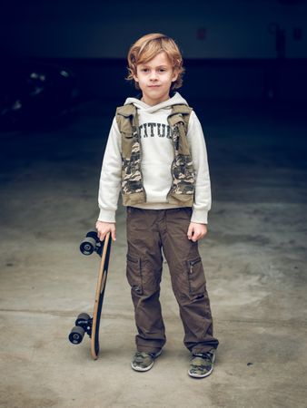 Child with skateboard standing on street