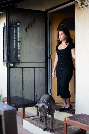 Beautiful woman standing at front door looking out with her dog nearby
