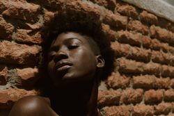 Young Black woman with eyes closed against wall