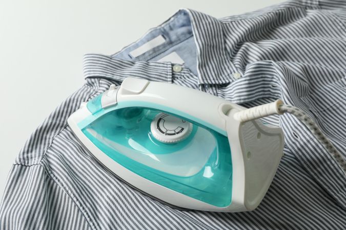 Iron and shirt on blank background, space for text