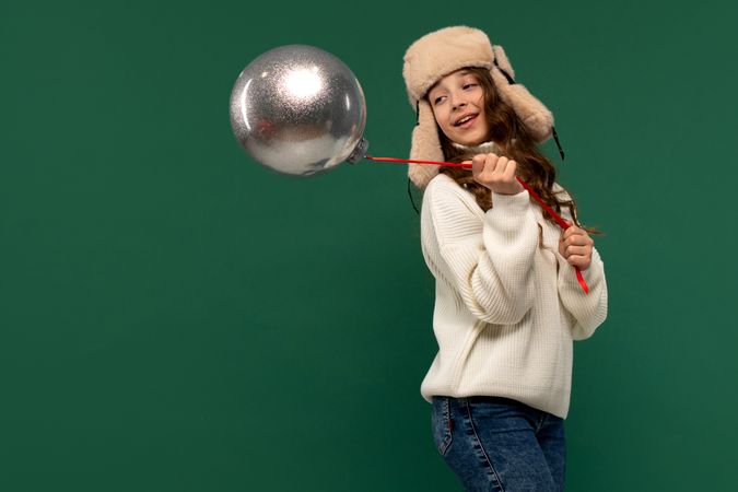 Playful girl swinging large silver ornament on red ribbon.