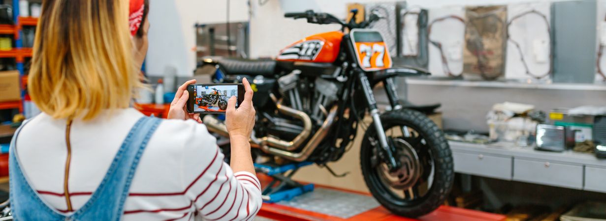 Female mechanic taking photo to motorcycle repaired over platform on garage