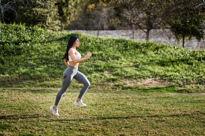 an athletic woman running in a park with her hair down in profil