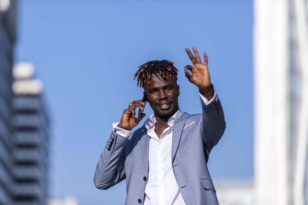 Black man wearing elegant suit standing in the street while looking in the distance in sunny day